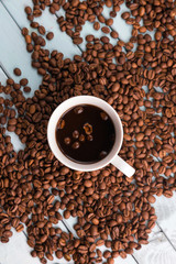Coffee beans are spilled on the wooden table. White coffee Cup. Top view of the still life. Turquoise boards.
