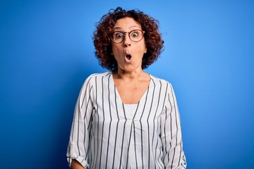 Fototapeta na wymiar Middle age beautiful curly hair woman wearing casual striped shirt over isolated background afraid and shocked with surprise expression, fear and excited face.