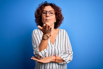 Fototapeta na wymiar Middle age beautiful curly hair woman wearing casual striped shirt over isolated background looking at the camera blowing a kiss with hand on air being lovely and sexy. Love expression.
