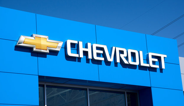 Chevrolet writing and logo on dealership bulding over blue sky.