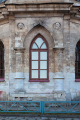 A picturesque window of an old Orthodox church framed by a voluminous frame with columns and faces of saints
