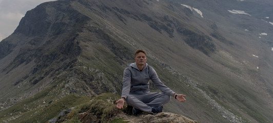 Young man meditates on the top of Alpine mountains.