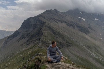 Naklejka na ściany i meble Young man meditates on the top of Alpine mountains.
