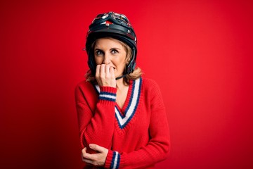 Obraz premium Middle age beautiful blonde motorcyclist woman wearing moto helmet over red background looking stressed and nervous with hands on mouth biting nails. Anxiety problem.