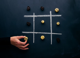 dark and white chocolate perlines on a tic tac toe board with a hand
