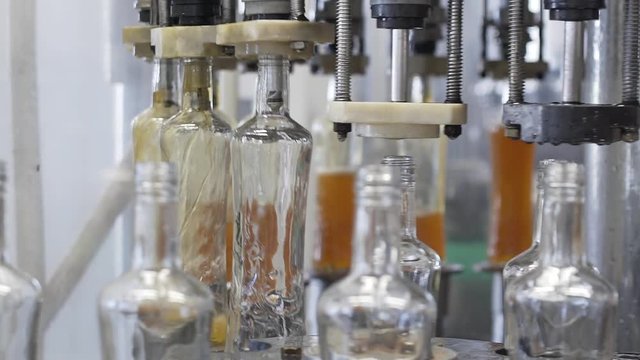 Slow motion of spill of brendy in glass bottles at distillery. Glass bottle filling machine in factory. Spillage of alcoholic beverages. Production process of alcoholic beverages in modern factory.