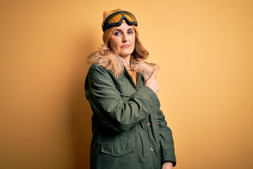 Middle age beautiful blonde skier woman wearing snow sportwear and ski goggles Pointing with hand finger to the side showing advertisement, serious and calm face