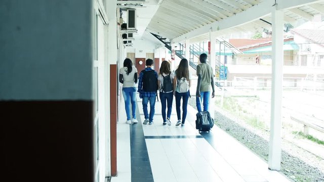 Group of five multi ethnic teenager students walking in school hallway, back view. Slow motion