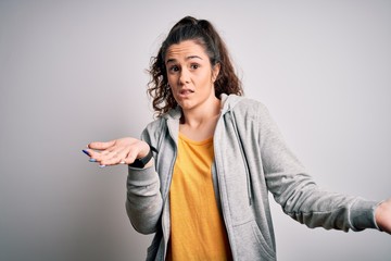 Young beautiful sportswoman with curly hair wearing sportswear over white background clueless and...