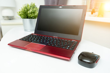 A modern red laptop and a mouse standing on white table, working space for business