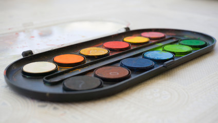 Colors on watercolor palette closeup. Selective focus. Black, blue, brown, red, yellow, green, orange colors on palette.