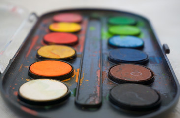 Obraz na płótnie Canvas Colors on watercolor palette closeup. Selective focus. Black, blue, brown, red, yellow, green, orange colors on palette.