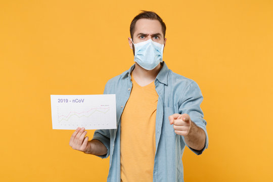 Strict young man in sterile face mask isolated on yellow background. Epidemic pandemic coronavirus 2019-ncov sars covid-19 flu virus concept. Hold infographic recovery death pointing finger on camera.