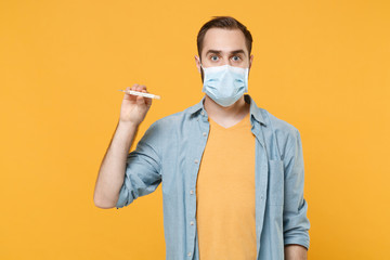 Young man in sterile face mask posing isolated on yellow wall background studio portrait. Epidemic...