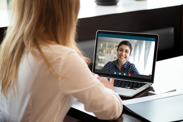 Fototapeta na wymiar Laptop screen view over female shoulder, businesswomen working from home on common project, company representative and client communication. Diverse girls friends chat via video conference application