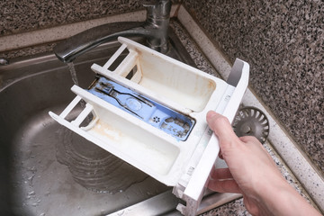 A person cleaning dirty moldy washing machine detergent and fabric conditioner dispenser drawer compartment. Mold, rust and limescale in washing machine tray. Home appliances periodic maintenance