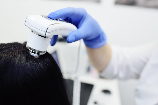 doctor dermatologist diagnoses the structure of the hair of a young pretty girl with a special tool - a trichoscope. Trichology, trichogram