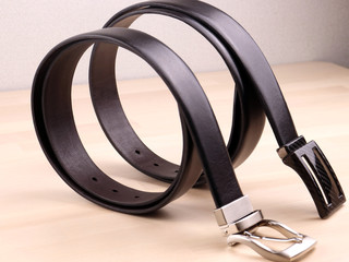 two stylish leather belts, beautifully folded in circles, on a light wooden surface. An expensive gift option for men, women, premium leather, chic performance, 