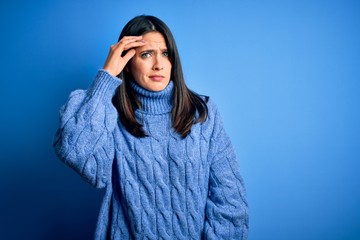 Young brunette woman with blue eyes wearing casual turtleneck sweater worried and stressed about a problem with hand on forehead, nervous and anxious for crisis