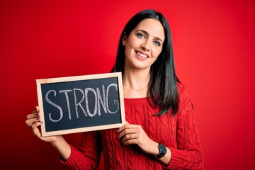 Young brunette woman with blue eyes holding blackboard with strong word message with a happy face standing and smiling with a confident smile showing teeth