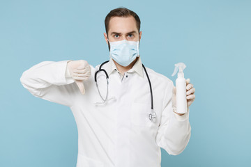 Doctor man in gown face mask gloves isolated on blue background. Epidemic pandemic coronavirus 2019-ncov sars covid-19 flu virus. Hold bottle alcohol liquid antibacterial sanitizer showing thumb down.