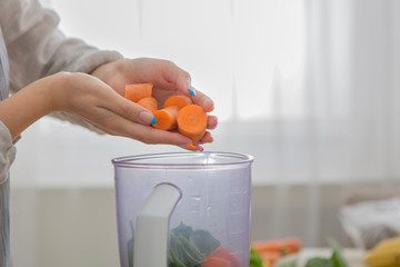 Woman blending carrot and other vegetables to make a healthy smoothie