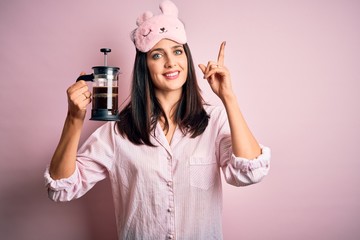 Young brunette woman with blue eyes wearing pajama making coffee with french coffeemaker surprised...