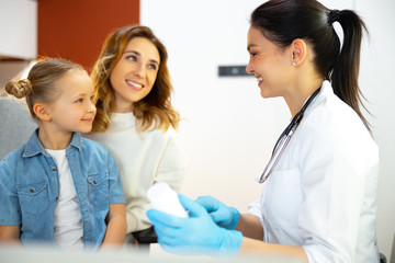 Fototapeta premium Little kid sitting on knees of her mother and listening to doctor