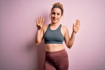 Young beautiful blonde sportswoman doing sport wearing sportswear over pink background showing and...