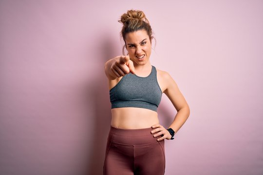 Young beautiful blonde sportswoman doing sport wearing sportswear over pink background pointing displeased and frustrated to the camera, angry and furious with you