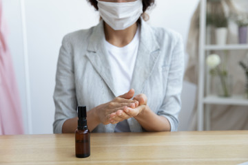 Young female employee worker businesswoman wearing facial virus protective gauze mask, sanitizing hands with antibacterial spray before workday start, covid19 coronavirus world outbreak protection.