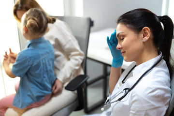 Tired female doctor with stethoscope on shoulders having rest