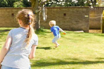 Fototapeta premium Children playing outside a brother and sister play a ball game in a garden