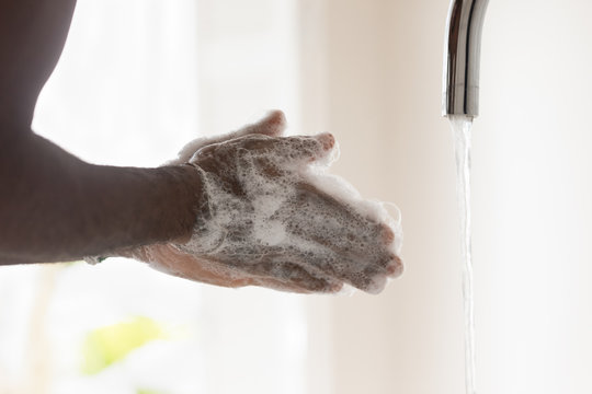 Side view close up young african american man washing hands with bubble antibacterial soap under tap water, preventing virus spreading or killing bacterium, morning routine, healthcare habit.