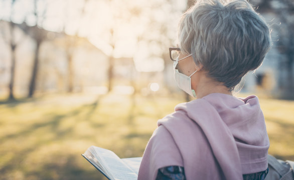 Senior Lady With Face Mask Reading The Bible In Front Of A Church