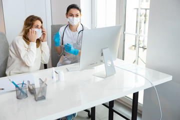 Fototapeta premium Caucasian women in medical mask looking at screen of laptop in hospital
