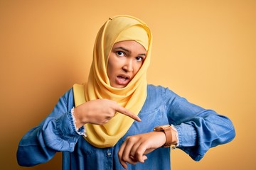 Young beautiful woman with curly hair wearing arab traditional hijab over yellow background In...