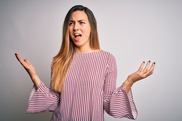 Young beautiful blonde woman with blue eyes wearing stiped t-shirt over white background crazy and mad shouting and yelling with aggressive expression and arms raised. Frustration concept.