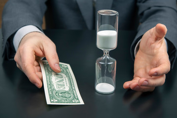 money and hourglass on the background of a business man. distribution of time for work. time to make decisions. human remuneration