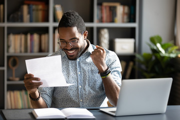 Overjoyed African American male student feel euphoric read good news in paperwork letter, excited biracial man triumph get positive answer reply in paper postal correspondence, success concept - obrazy, fototapety, plakaty
