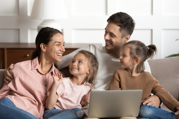Joyful full family spending weekend leisure time with computer, communicating in living room. Happy...