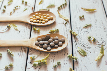 Herbal pills and dry herbs on wooden background.
