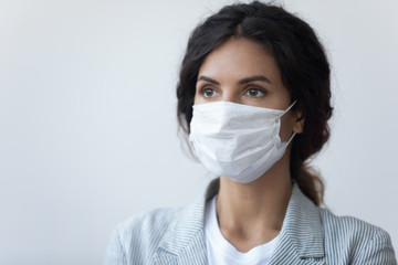 Head shot young brunette woman covering mouth and nose with special facial medical equipment, looking away. Serious lady wearing medical mask, protecting breath from air pollution or virus infection.