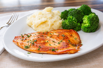 A view of a plate of grilled salmon, steamed broccoli and mashed potatoes, in a restaurant or kitchen setting.