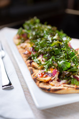 A view of a flatbread appetizer with grilled chicken and deep fried arugula, in a restaurant or kitchen setting.