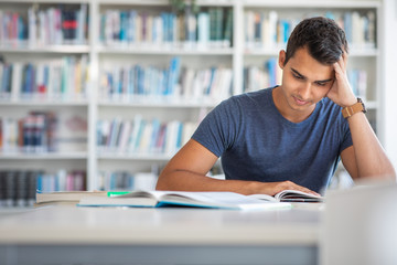 Students in a library - handsome student reading a book for his class in a bright modern library