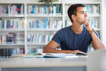 Student in a library - handsome student reading a book for his class in a bright modern library