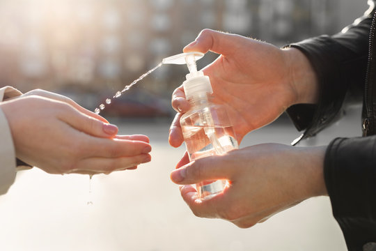 Antiseptic For Hands. Fighting Viral Diseases For Prevention. A Man Applies An Antiseptic Hand Spray To A Woman's Hands In The Fight Against The Covid 19 Coronavirus