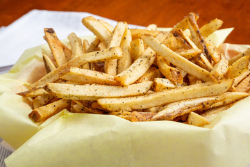 A closeup view of a carton of french fries on a plate, in a restaurant or kitchen setting.