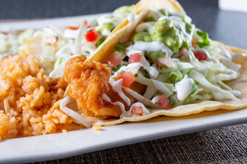 A closeup view of a Baja style fish taco plate, in a restaurant or kitchen setting.